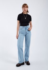 Camiseta negra de manga corta combinada con jeans de mezclilla de cintura alta en un tono azul claro. La modelo lleva zapatos de plataforma negros y gruesos, así como collares de plata en capas.