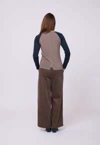 Maglietta a maniche lunghe con un torso aderente marrone e maniche blu scuro, abbinata a pantaloni in corda a gamba larga con un motivo a righe verticali marroni.