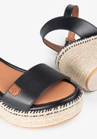 Las sandalias de cuero negro cuentan con una tira ancha, una suela de plataforma de fibra natural y un acento de cuerda texturizada con un detalle de costura negra en contraste.