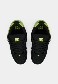 Schwarze Sportschuhe mit grünen Akzenten, strukturiertem Obermaterial und auffälligen Logos an Zunge und Seiten, mit niedrigem Profil und Schnürdesign.