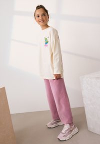 Cream long-sleeve shirt with colorful cartoon graphic, paired with soft pink fleece pants and light pink sneakers with contrasting accents.