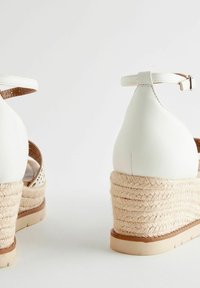 Sandalias de cuña de cuero blanco con tacón de yute trenzado, que incluyen una delgada correa para el tobillo y detalles recortados en los lados.