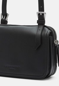 Borsa a tracolla in pelle nera con chiusura a zip, tracolla regolabile e logo in rilievo. Presenta una texture liscia e un design rettangolare minimalista.
