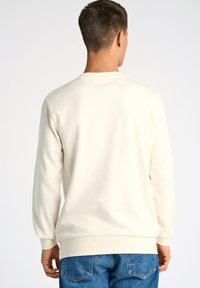 Vit, lätt sweatshirt med långa ärmar, ribbade muddar och rundad halsringning, i kombination med blå denimjeans. Slät textur, minimalistisk design.