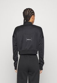 Svart kort sweatshirt med hög krage och långa ärmar. Har en minimalistisk logotyp i vitt på baksidan och är tillverkad av mjukt material.