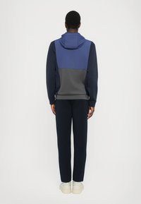 Hoodie s podešavom kapom u kombinaciji mornarske i sive boje, s elegantnim dizajnom i usklađenim mornarskim hlačama. Glatka tekstura, ležeran stil.