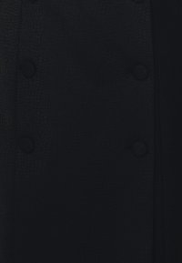 Mörk marinblå texturerad tyg med knappstängning och släta detaljer. Ytan har ett subtilt mönster som ger djup åt designen.