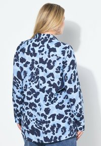 Lichtblauwe shirt met een donkerblauwe luipaardprint, lange mouwen en een kraag. De achterkant toont een yoke en een rechte zoom.