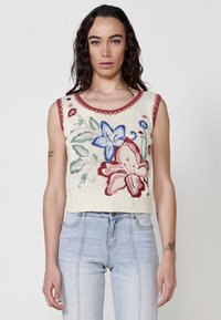 Top sin mangas de punto en color crema con bordado floral multicolor (azul, rojo, verde) y un escote rojo con forma de ondulación. Diseño ajustado, patrón texturizado.