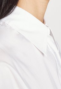 Camicia bianca con un tessuto liscio e pulito. Presenta un colletto classico, che sottolinea un aspetto elegante e minimalista.