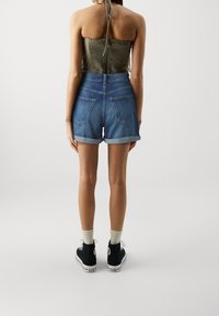 Denim shorts with a high waist, rolled cuffs, and two back pockets, paired with a ribbed olive top and black sneakers with white soles.