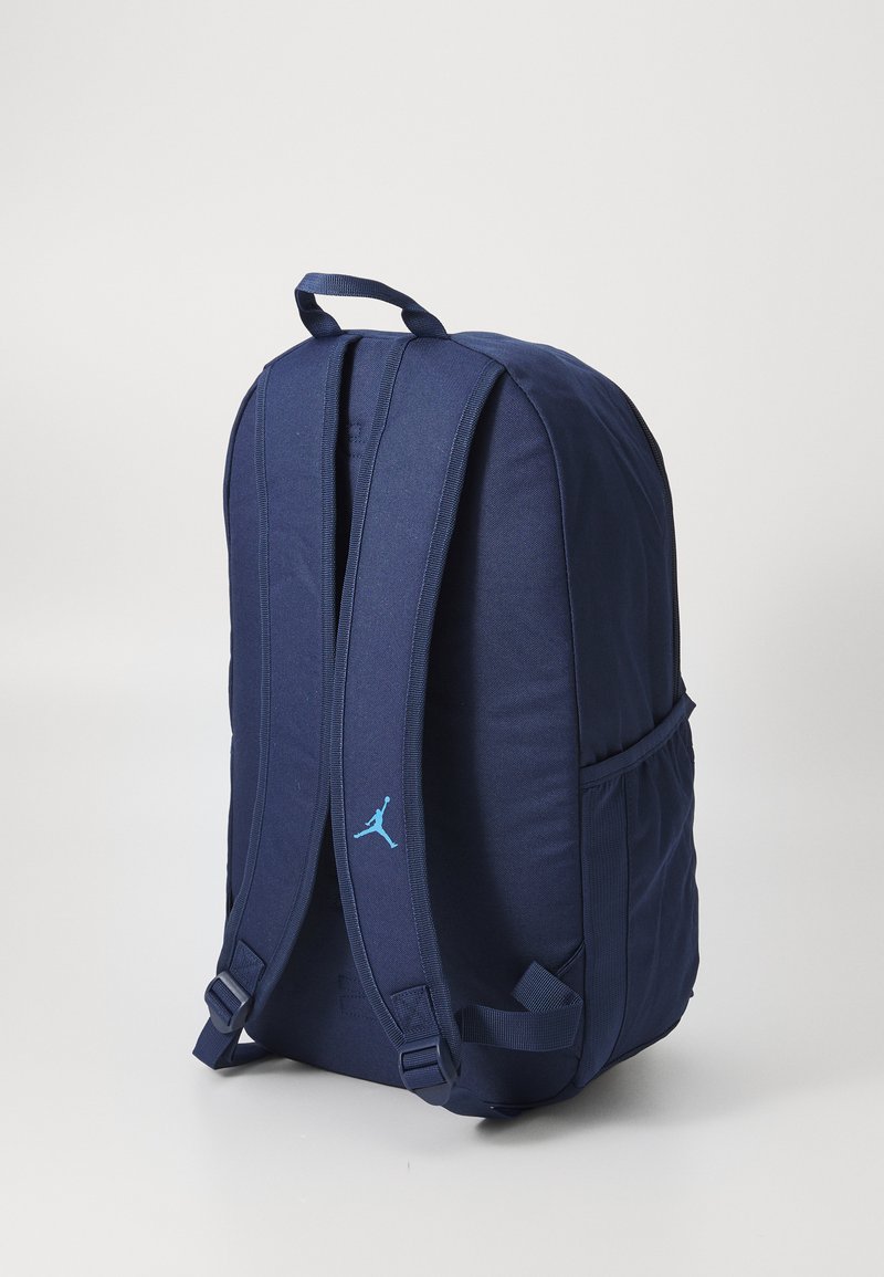 Mochila azul marino con correas acolchadas, tela texturizada y un diseño ligero. Presenta un logo de acento en gris azulado en la parte frontal.