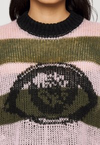Gebreide trui met een zwarte ribbelkraag, open weving en horizontale strepen in olijfgroen en lichtroze, met een zwart rond patroondetail.