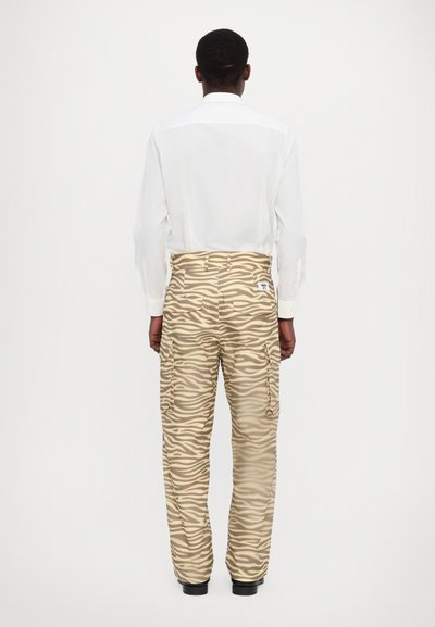 Beige cargobroek met een zebra-strip patroon, voorzien van zijzakken en een iets relaxte pasvorm. Gladde textuur en details van de tailleband zichtbaar.