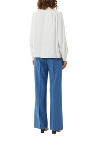 Biała jedwabna bluzka z marszczonymi ramionami, zestawiona z niebieskimi spodniami o szerokich nogawkach. Gładka tekstura i luźny krój, odpowiednie na różne okazje.