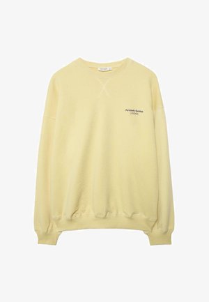 Lichtgele crewneck-trui met geribbelde manchetten en zoom, met kleine zwarte tekst "Portobello Sundays LONDON" op de linkerborst.