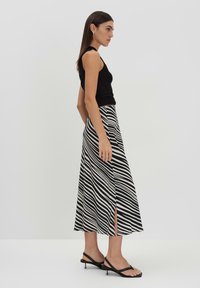 Top nero senza maniche abbinato a una lunga gonna a strisce in bianco e nero con spacchi laterali. La modella indossa sandali neri con i lacci.