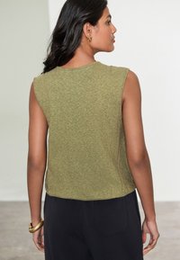 �Ærmeløs top i olivengrøn i blødt stof, cropped design med rund hals. Enkel, tekstureret finish med afslappet pasform. Sorte bukser er synlige.