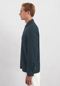Dunkelblaues Langarmhemd mit Knopfverschluss, einer einzelnen Brusttasche und Knöpfen an den Manschetten. Aus leichtem Stoff gefertigt.