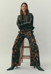 Fekete bőr bombázó dzseki elöl cipzárral, laza barna állatmintás nadrággal és fekete, hegyes orrú bokacsizmával párosítva.