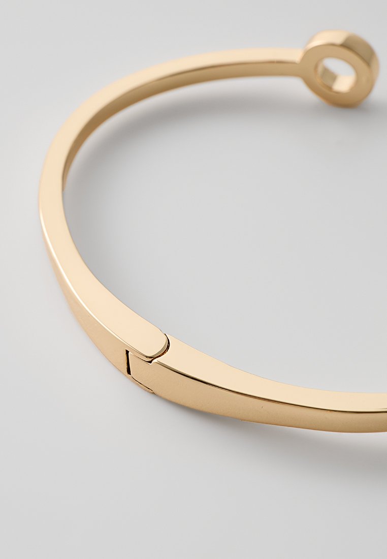 Goldplätierter Armreif mit einem eleganten, geschwungenen Design und einem verbundenen offenen Ring. Glatte, reflektierende Oberfläche mit minimalen Hardware-Details.