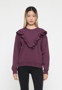 Sweatshirt violet avec un design froncé en V le long de l'encolure, des manches longues et une taille ajustée. Fabriqué en tissu doux.