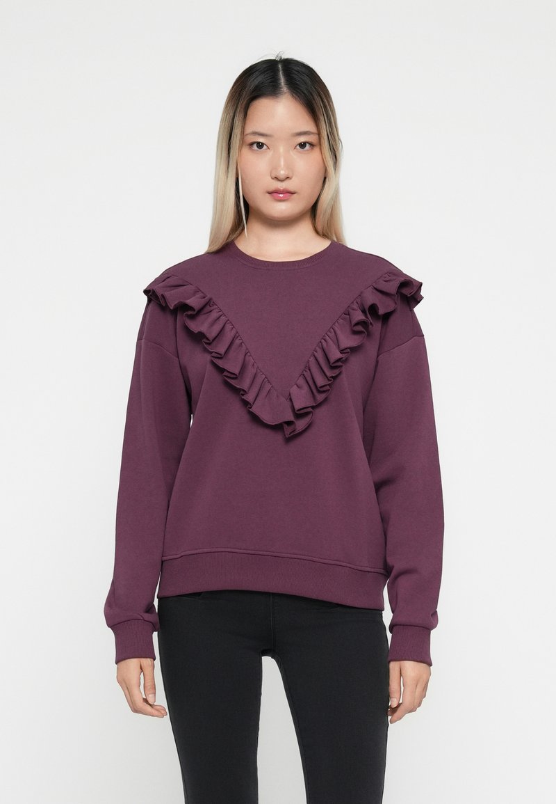 Sweatshirt violet avec un design froncé en V le long de l'encolure, des manches longues et une taille ajustée. Fabriqué en tissu doux.