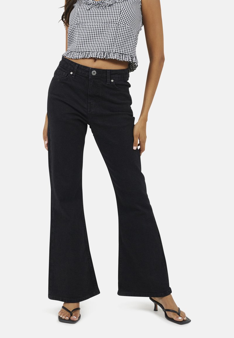 Jean noir évasé en denim, avec une taille haute, un design à cinq poches et des détails de couture subtils. Porté avec un crop top à carreaux.