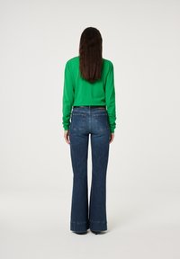 Groene lange mouw top gecombineerd met blauwe flare jeans, met een hoge taille en subtiele achterzakken. Glad, gestructureerd stof.