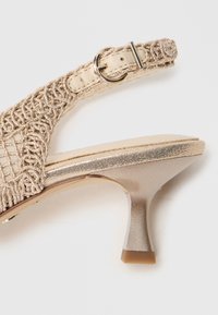 Μπεζ σανδάλι με ψηλό τακούνι που διαθέτει πλεκτό επάνω μέρος, μεταλλικές λεπτομέρειες, λουράκι με αγκράφα και υφαντό τακούνι.