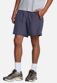 Shorts de sport pour hommes, gris foncé, avec poches latérales, taille élastique, en tissu léger, associés à des chaussures de trail gris et olive.