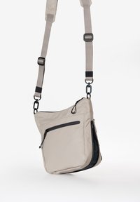 Beige Umhängetasche mit strukturiertem Obermaterial. Verfügt über graue Akzente, einen verstellbaren Riemen und mehrere Reißverschlusstaschen zur Aufbewahrung.