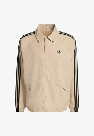 Beige jacket with black side stripes, snap buttons, and two front pockets; features a pointed collar and an embroidered logo on the chest.
