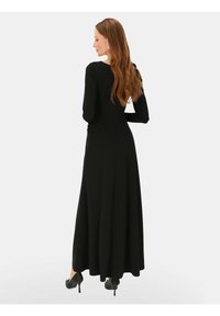 Czarna sukienka maxi z długim rękawem, dopasowaną górą i luźnym dołem, wykonana z miękkiego materiału, z okrągłym dekoltem i subtelnymi detalami szwów.