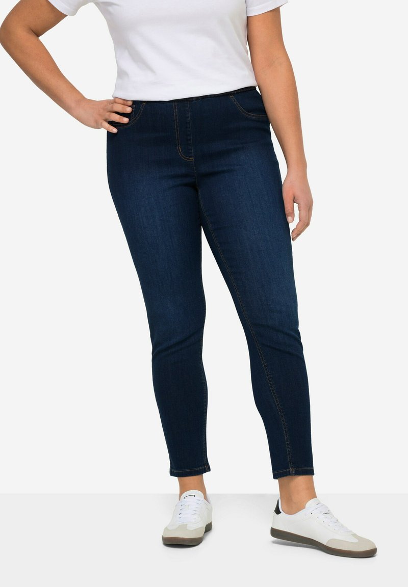 Jeans skinny azul oscuro hechos de denim, con un diseño ajustado y sutilezas en las costuras. Combinados con zapatillas blancas.