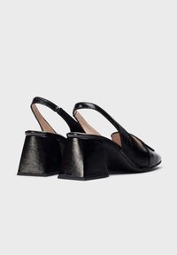 Des escarpins noirs à talons bloc bas avec une finition texturée, un design ouvert à l'avant et une sangle élégante à l'arrière.