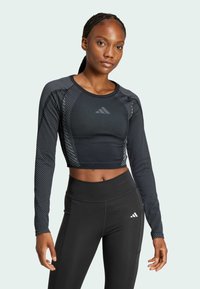 Crop top nero a maniche lunghe con texture orizzontale, impreziosito dal logo Adidas. Abbinato a leggings neri a vita alta, in tessuto liscio.