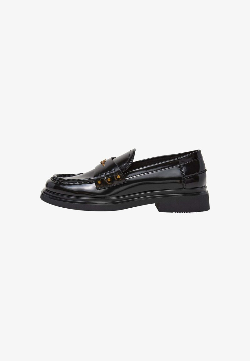 Mocassin en cuir noir brillant avec talon bas, clous dorés décoratifs sur la bride et coutures détaillées sur l’avant et les côtés.