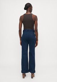 Mørkeblå vide bukser med høj talje, denimtekstur og oprullede manchetter, parret med en tætsiddende brun tanktop og leopardmønstrede hæle.