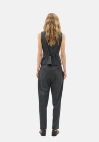 Šedý formálně střižený bezrukávový top s peplum detailem a mašlí na zadní straně, doplněný volnými šedými nohavicemi a černými botami.