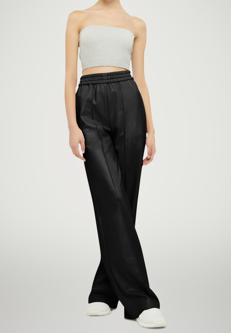 Femme portant un crop top gris sans bretelles, un pantalon large noir taille haute avec une taille élastique, et des chaussures blanches slip-on, debout.