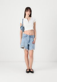 Witte, geribbelde, cropped t-shirt met een kraag en silberen rits. Lichtblauwe denim shorts met rafelige randen. Zwarte schoenen met studaccenten.