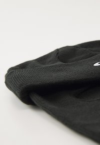 Black knitted beanie with a folded brim lying flat on a light surface, showing knit texture and partial embroidered logo.