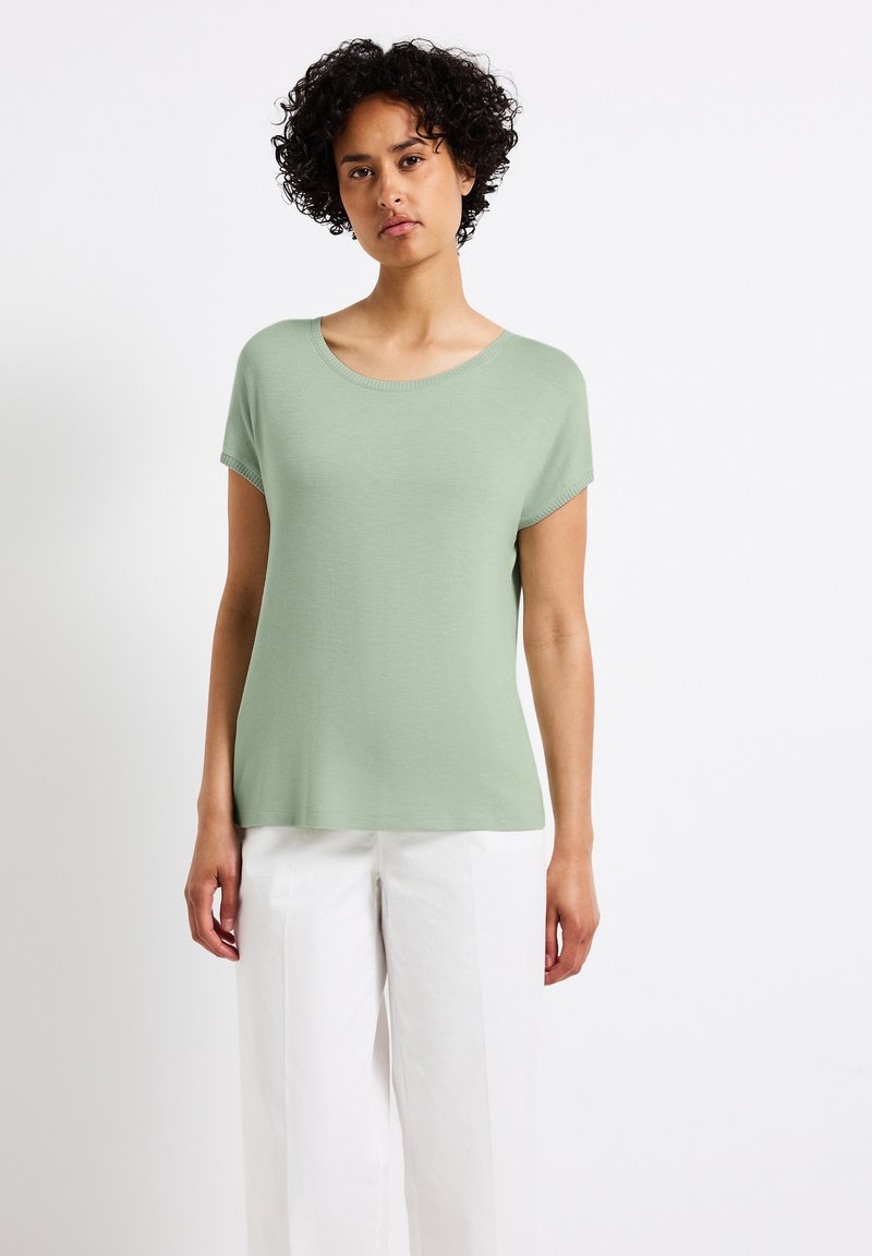 Lichtgroen T-shirt met korte mouwen en een ronde halslijn, gemaakt van een gladde stof, gecombineerd met witte wijde broek. Eenvoudig, casual ontwerp.