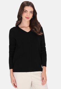 Fekete bordázott kötött pulóver V-kivágással és hosszú ujjakkal, középen varrási részlettel. Világos színű nadrággal párosítva.