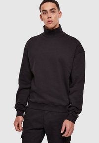 Svart genser med høy hals laget av mykt materiale og avslappet passform, med lange ermer og ribbestrikkede mansjetter og kant.