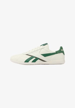 Zapatilla Reebok blanca de corte bajo con rayas verdes y lengüeta en el talón, suela texturizada y cordones, mostrada de perfil hacia la derecha.