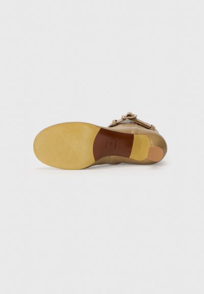 Beige lädersko med rund tå och platt gummisula. Har en dekorativ rosett på sidan och en slät yta.