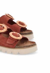 Sandales en daim rouge avec deux larges brides et de grands accents circulaires. Semelle épaisse et claire avec une base en brown texturée.