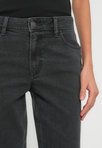 Čierne rifľové nohavice s rovno strihanými nohavicami, so zapínaním na gombík a zips, pútkami na opasok a prednými vreckami. Materiál má miernu textúru.